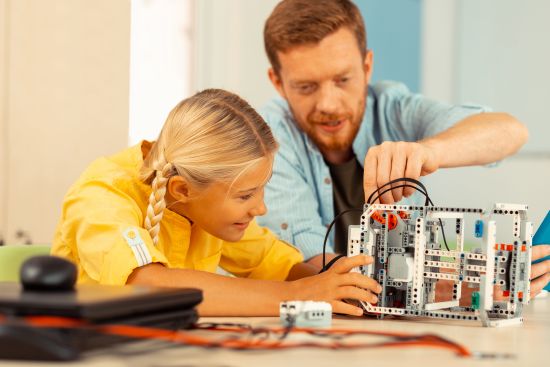 cheerful-girl-looking-at-her-teacher-building-a-ro-2022-01-27-21-24-53-utc